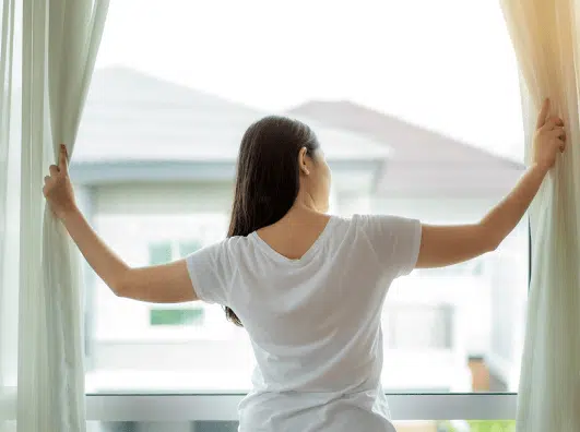 Woman opening curtains to enjoy natural light in a cozy indoor setting, highlighting a peaceful morning routine.