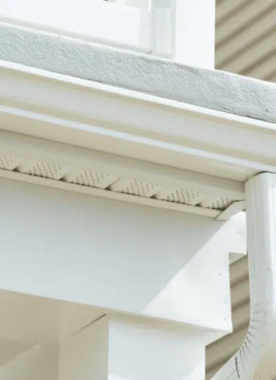 Close-up view of a white gutter system and fascia board on a residential home, highlighting the perforated design for effective water drainage and prevention of debris buildup.