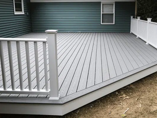 Composite deck with white railing and gray surface, set against a green siding backdrop, showcasing a spacious outdoor area. Ideal for home improvement and landscaping projects.