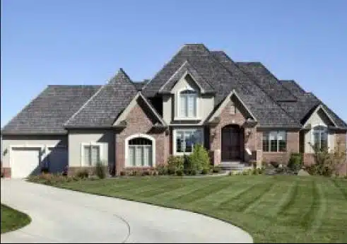 Elegant suburban home with a large driveway, manicured lawn, and a combination of brick and stucco exterior under a clear blue sky.